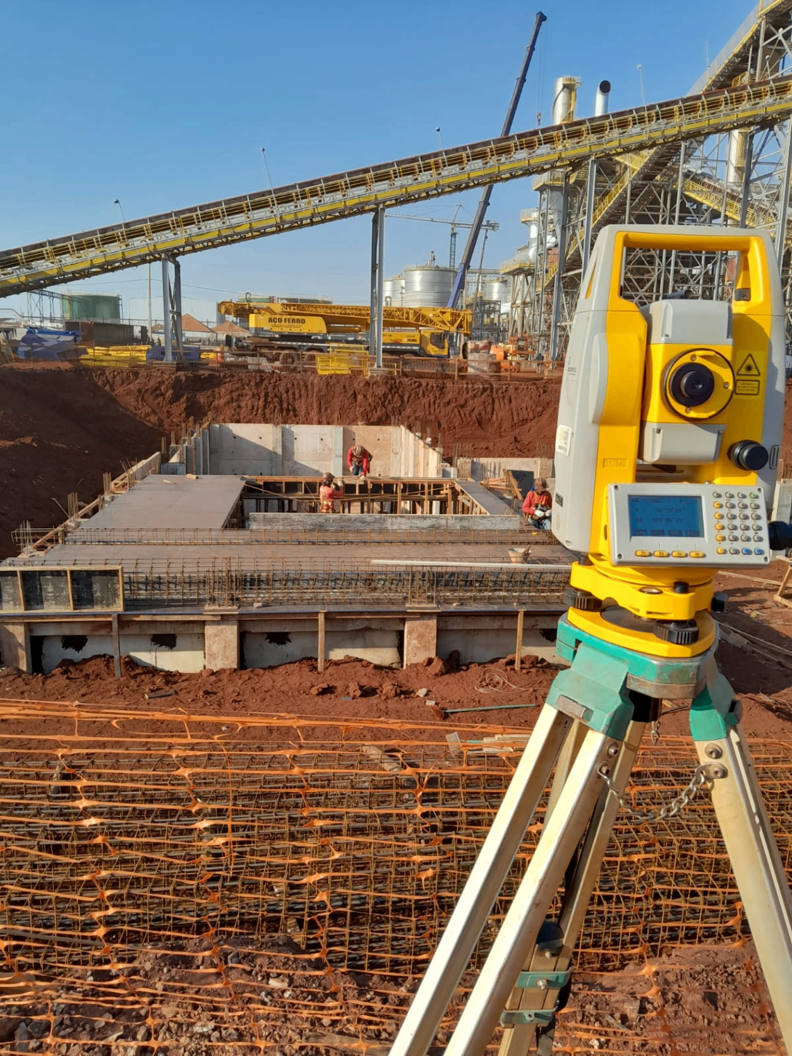 Equipamento topográfico monitorando obra civil com armação e concreto em execução.